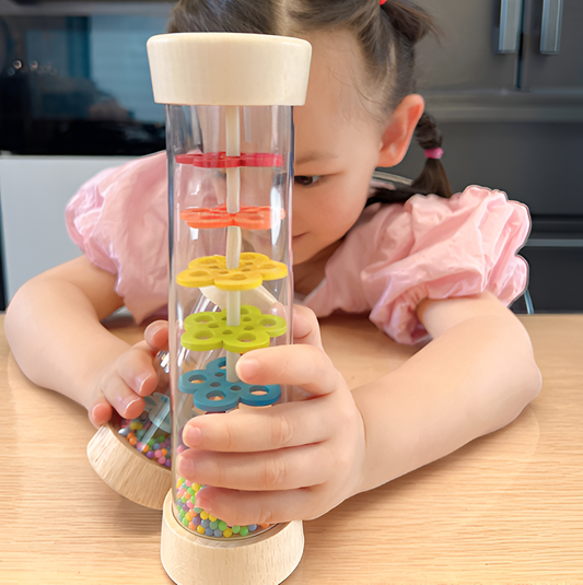 Child playing with a Montessori Wooden Toddler Rattle, designed to stimulate sensory exploration, fine motor skills, and auditory development through hands-on play.